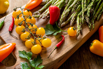 Various vegetables, asparagus, cherry tomatoes, with sweet and hot peppers on a wooden board on a wooden background. photo in a dark key.fresh spring food. proper nutrition. - 773868800
