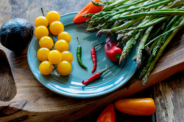 Various vegetables, asparagus, cherry tomatoes, with sweet and hot peppers on a wooden board on a wooden background. photo in a dark key.fresh spring food. proper nutrition.