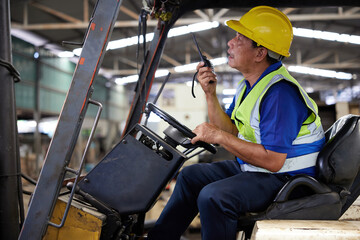 senior worker using walkie talkie and driving forklift truck in the factory