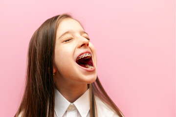 cheerful little teenage girl with braces screams loudly and announces on a pink isolated background, a child with an open mouth speaks