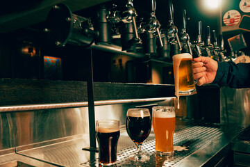 Photo of bartender pouring cold foamy beer from tap into glass at bar with multiple beer...