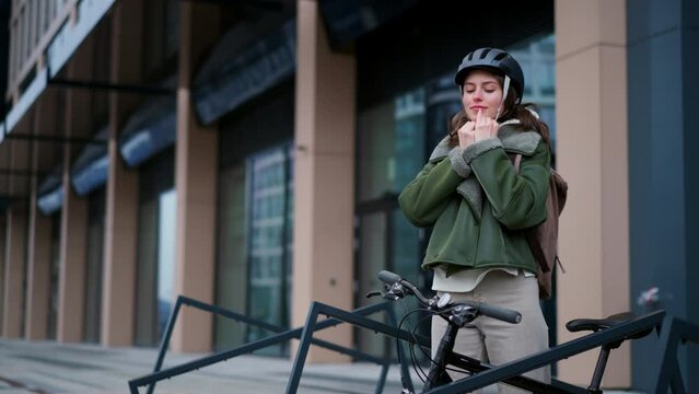Beautiful urban woman putting cycling helmet on head. Bike rack in front of office building, university. Concept of bike commuting in the city, sustainable lifestyle.