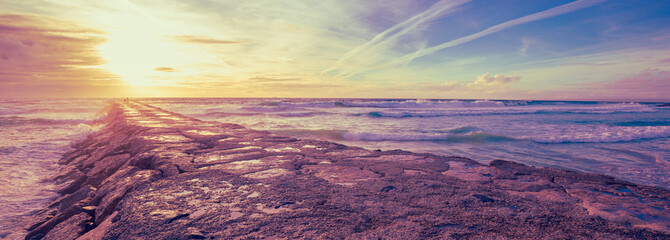 Sunset over the Atlantic Ocean. A stone breakwater in the ocean. Horizontal banner