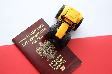 Red polish passport and yellow tractor on smooth red and white flag of Poland close up - obrazy, fototapety, plakaty