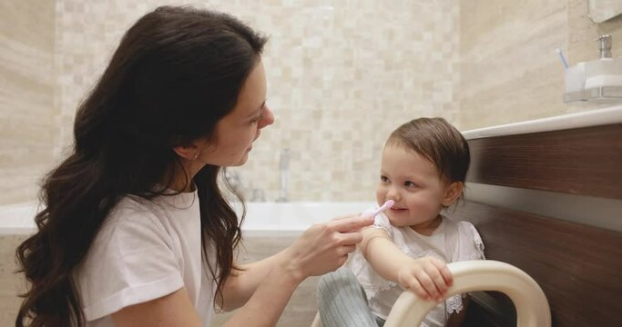 curly mother teaching baby girl brushing teeth with toothbrush. mother brushing her little daughters teeth in the bathroom