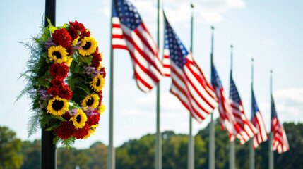 a row of American flags flying at half-staff, with a wreath of flowers in the foreground