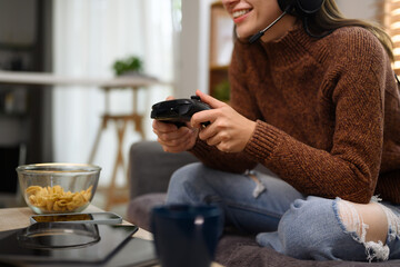 Happy smiling young woman wearing headset playing video game with joystick in living room