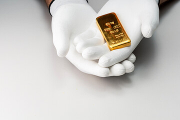 Male hands in white glove holding a gold bar.  Concept of buying gold bar or a saving money for...