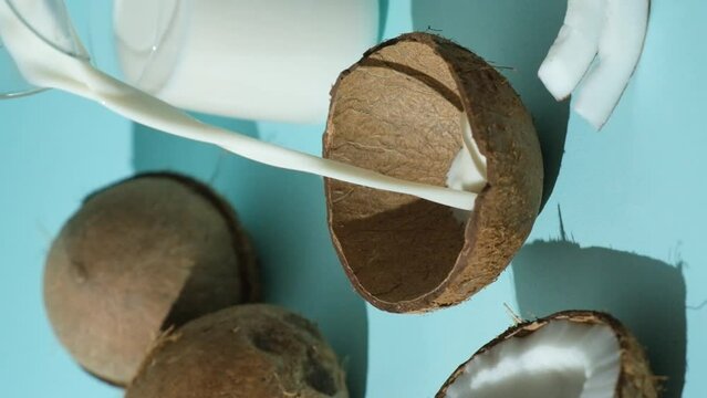 Healthy vegan coconut milk pouring in coconut shell on blue background. Vertical slow motion