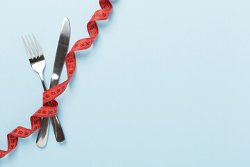 Measuring tape with fork and knife on wooden background, top, view.Weight loss concept