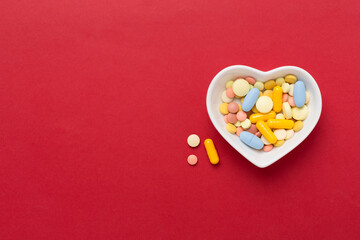 Medicines in heart-shaped bowl on color background, top view
