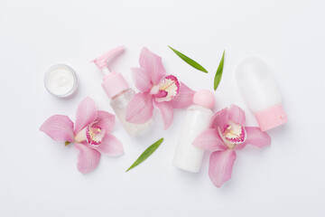 Bottles and jars with cream and orchids on color background, top view - obrazy, fototapety, plakaty