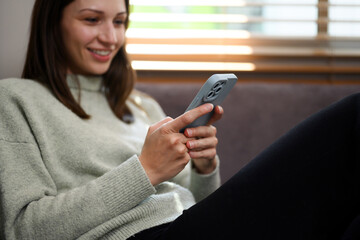 Happy caucasian woman relaxing on couch and using mobile phone