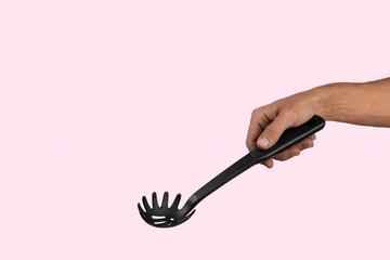 Black male hand holding plastic kitchen skimmer on light purple background.