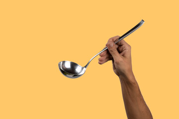 Black male hand holding a silver kitchen ladle isolated o yellow background