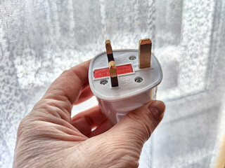 Close-Up of a Hand Holding a White Electrical Adapter. Hand displaying a UK-style three-pin...