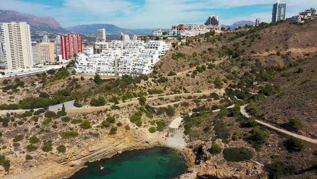 Aerial drone footage or the north part of Benidorm in Spain showing the rocky paths by the ocean in the summer time and the beach known as The Cala Tio Ximo Beach