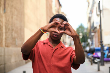 Gay black man in a red shirt is holding his hands together in the shape of a heart. Concept of homosexual love and affection.