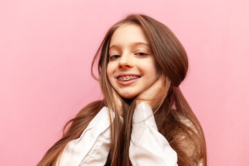 little teenage girl with braces smiling and holding long hair on pink isolated background, child...