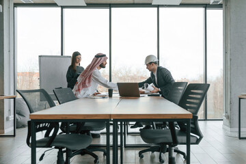 Working with a plan. Muslim businessman in traditional outfit with colleagues in office
