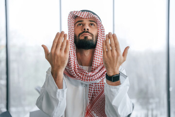 Praying with hands near the face. Successful Muslim businessman in traditional outfit in his office
