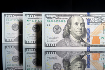 one hundred American dollar bills stand on a mirror surface on a black background