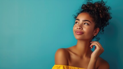 Beautiful young pretty mixed raced woman in a yellow dress before a solid blue colored background. She is thinking and smiling.