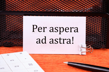 Per aspera as astra in English means through hardships to the stars on a clean white business card next to a calculator, a pen on an orange background