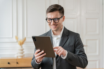 An executive dons a tailored suit, using a tablet with an engaging smile, set against a minimalist and sophisticated interior.