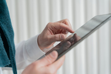 Close-up of a person's hands expertly navigating a tablet, with a glimpse of a teal scarf and white shirt indicating a smart, casual style.