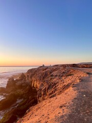 Golden sunset lights up the rocky coastline of Morocco, with the calm ocean meeting the warm, glowing sky.