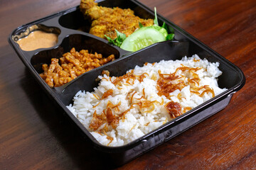 Indonesian meal box called uduk placed on the wooden table.