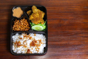 Indonesian meal box called uduk placed on the wooden table.