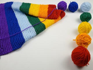 Colorful balls of wool for knitting, hand-knitted scarf in rainbow colors and knitting needles
