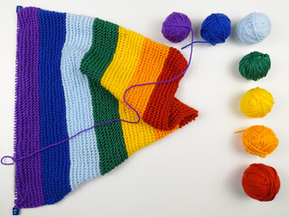 Colorful balls of wool for knitting, hand-knitted scarf in rainbow colors and knitting needles