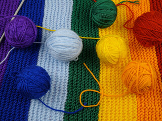 Colorful balls of wool for knitting, hand-knitted scarf in rainbow colors and knitting needles 