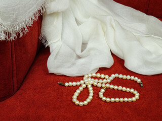 A white chiffon shawl and white pearl necklace lie on the seat of a red velour armchair