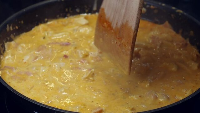 Hot pan of creamy chicken curry cooks on stove, stirred with spatula