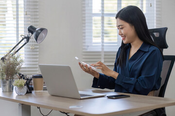 Asian businesswoman sitting and working using laptop in home office with cheerful smile.