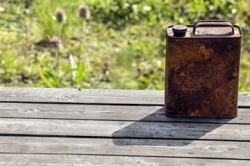 A rusted fuel cane sits on a table, its golden tones highlighted by sunlight.