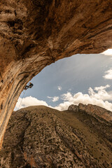 A man is climbing a rock wall with a rope. The sky is blue and there are clouds in the background
