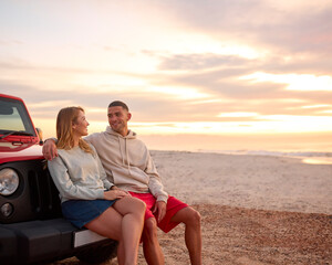 Young Couple Standing Chatting By Car At Beach Watching Sunrise Together