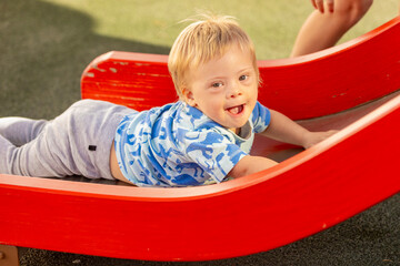 Joyful toddler with Down syndrome on playground slide
