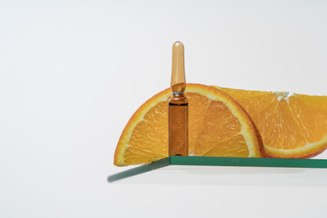 Vitamin C serum in ampoule with orange slices backdrop