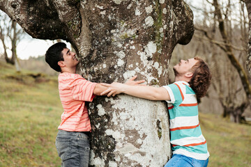 A heartwarming scene as a gay couple, both transgender men, share an affectionate embrace with a grand tree in a peaceful forest landscape