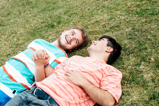 Two men, deeply in love and both transgender, enjoy each other's company, smiling and holding hands on a grassy field
