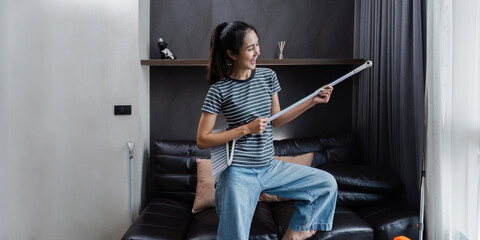 young asian woman having fun during cleaning, fooling with mop and broom