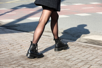 Female legs in black boots with shadow on pavement. Slim girl in pantyhose walking down a street, fashion in spring city