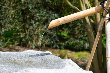 Clear water in a bamboo fountain. Street water source. Decorative garden structure with a stone...