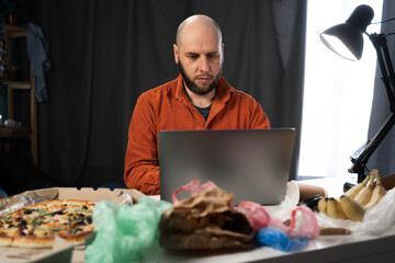 Portrait of focused man using laptop, typing on keyboard, chatting, working at home. Successful freelancer working online sitting in messy room